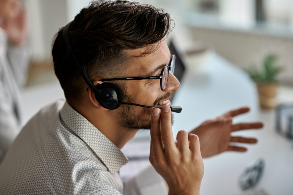 Homem usando fone de ouvido para falar por VOIP com seus clientes no escritório.
