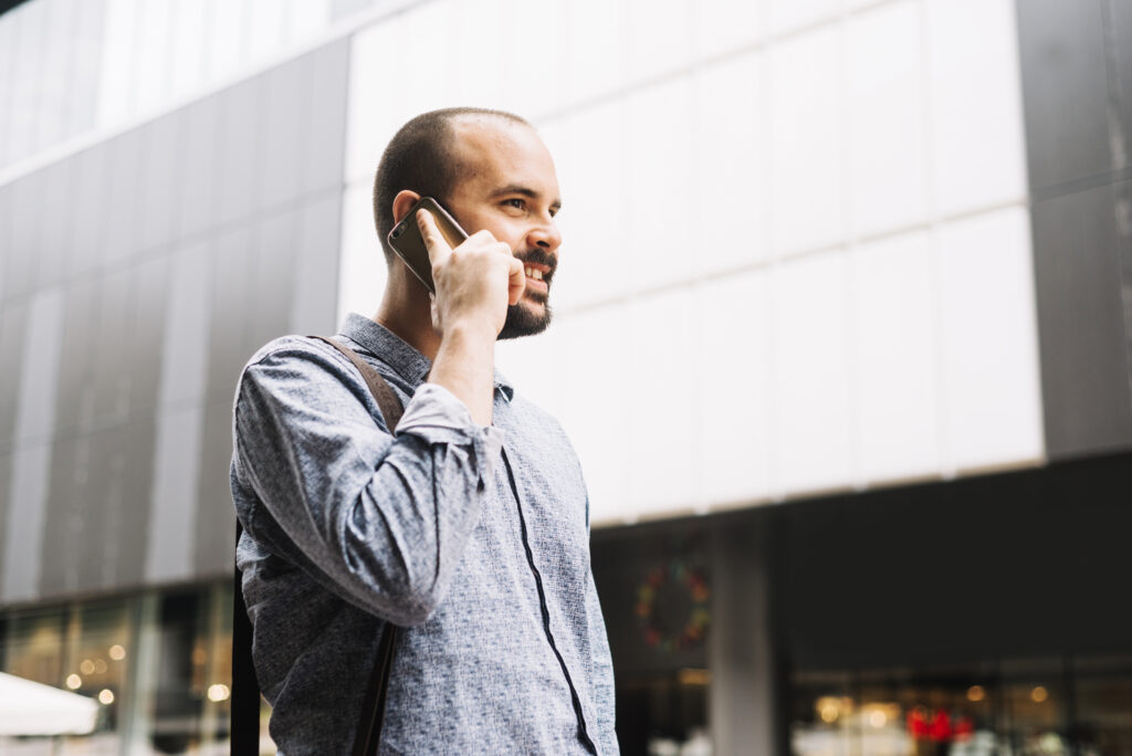 Homem vestido socialmente utilizando um celular para entrar em contato com alguém no trabalho.