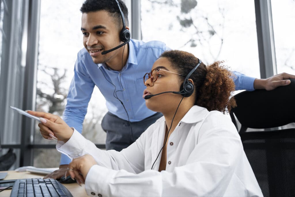 Colaboradora mexendo no computador com um headset enquanto recebe treinamento do seu gestor.